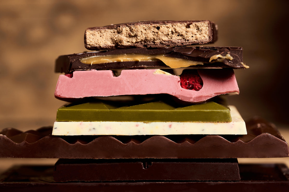 Stack of 7 layered chocolate bars in different colors and flavors against a blurred background. 