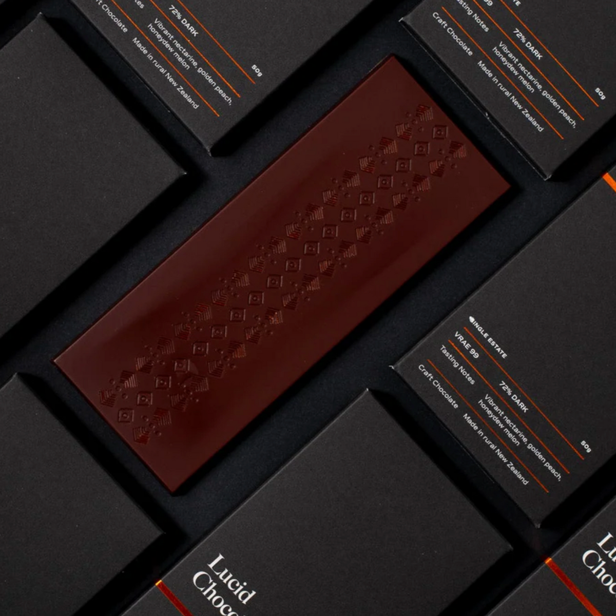 Unwrapped dark chocolate bar set against a dark surface and surrounded by wrapped Lucid Chocolatier bars.