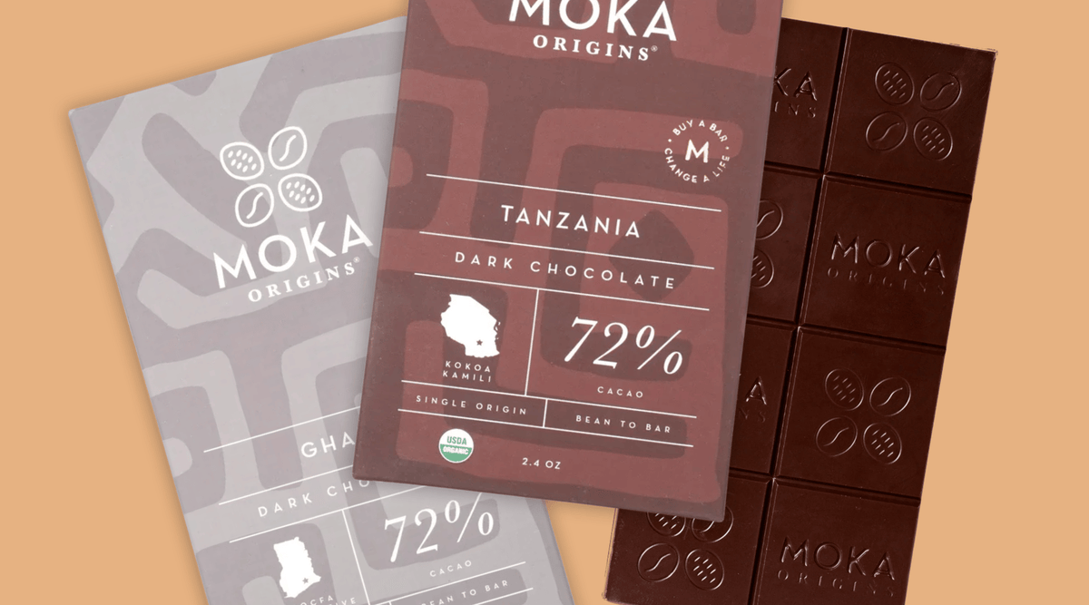 Moka Origins Tanzania 72% dark chocolate packaging shown with a gray chocolate bar packaging and a dark brown chocolate bar on a warm beige background.