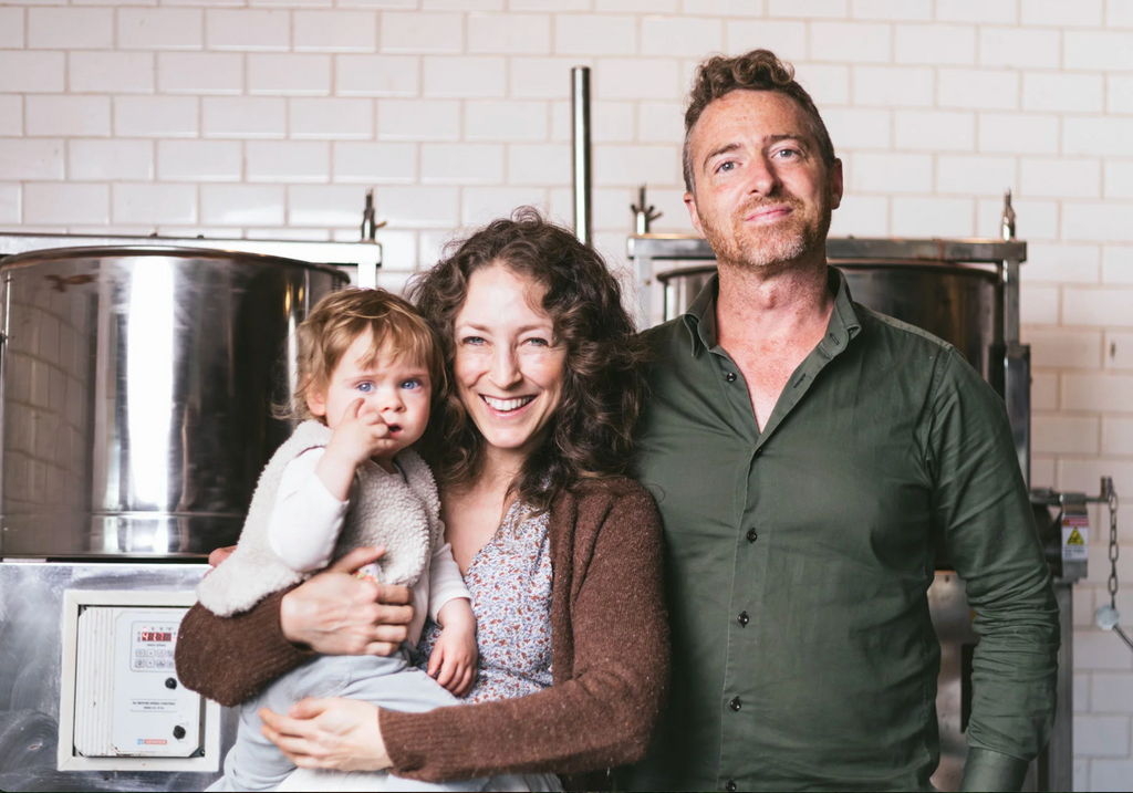 A picture of the founders of Crow and Moss chocolate with their baby in front of pots on a stove