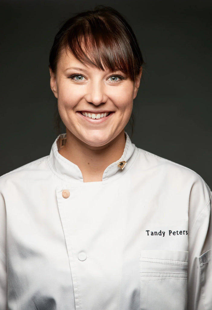 Founder of Ember Chocolate Tandy Peterson in a chef coat smiling in front of a dark grey background
