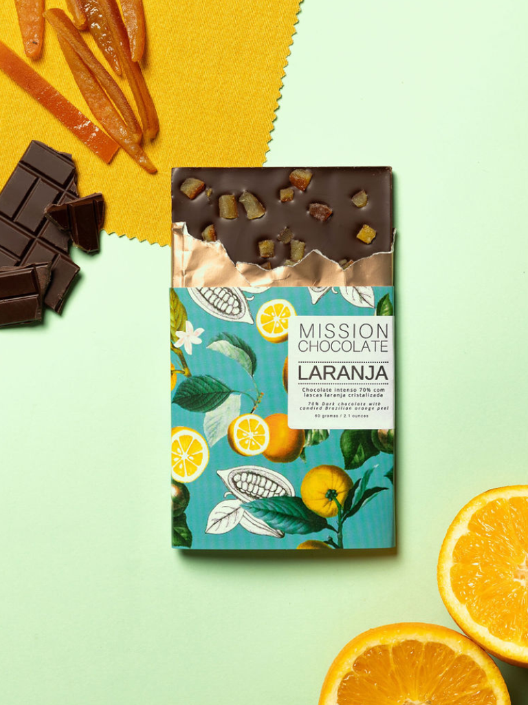 Partially opened Orange Dark Chocolate 70% bar on agreen table with chocolate ingredients