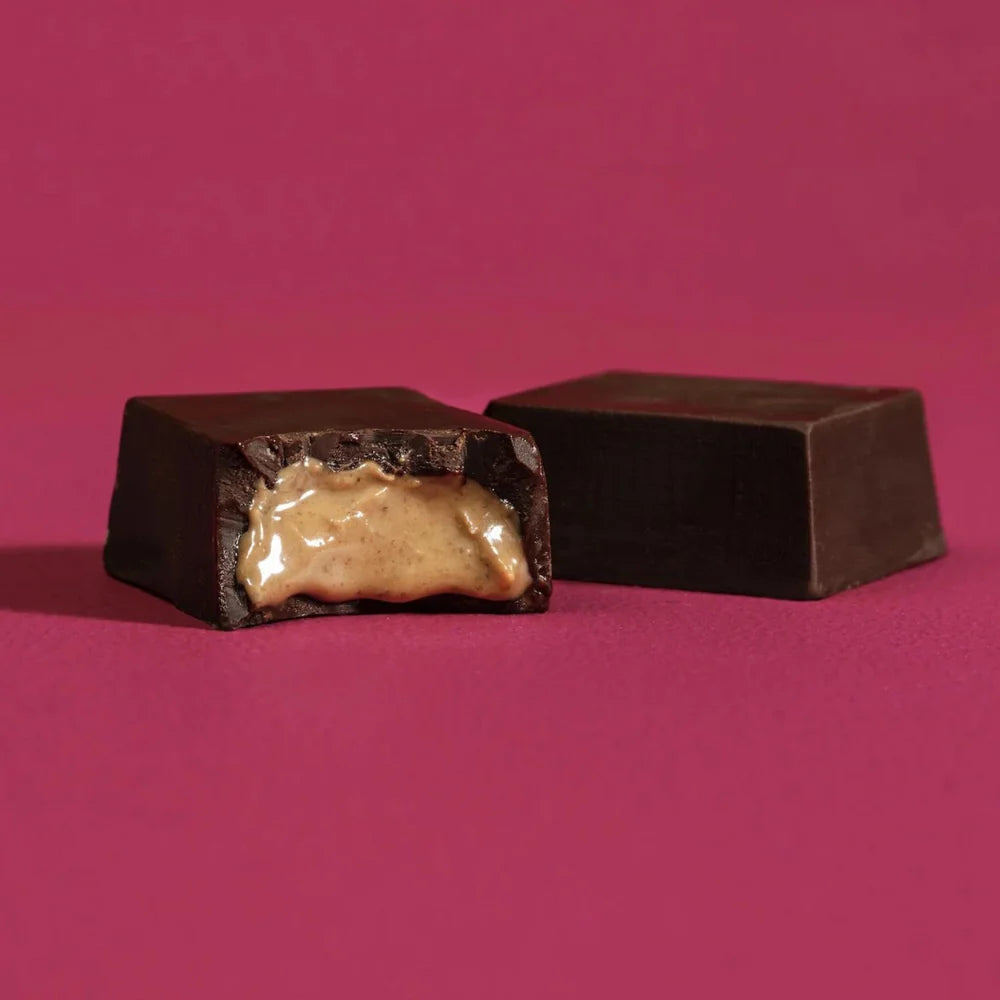 Two unwrapped pieces of a Almond Butter Bar against a dark pink background