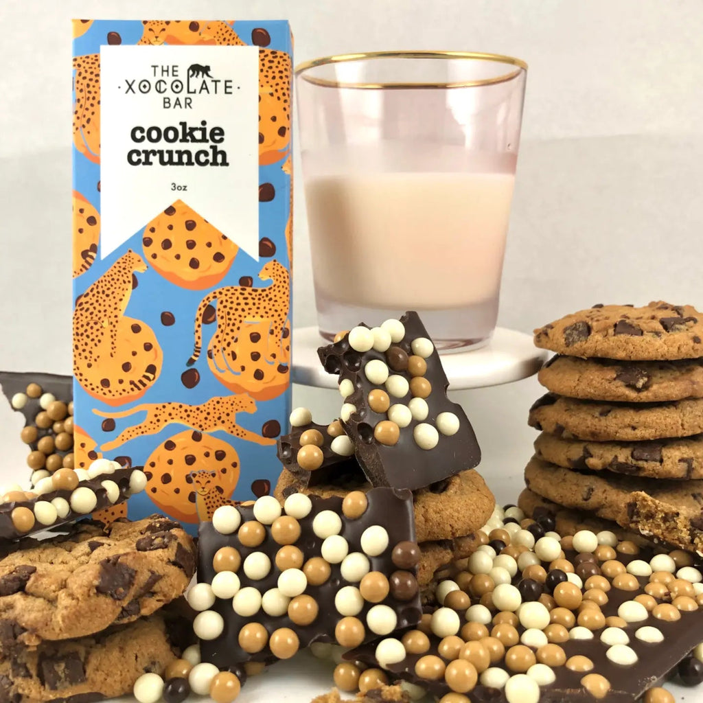 The Xocolate Bar Cookie Crunch - Dark Milk and White Chocolate Bar with cookies, unwrapped bars, and a glass of milk against a white background