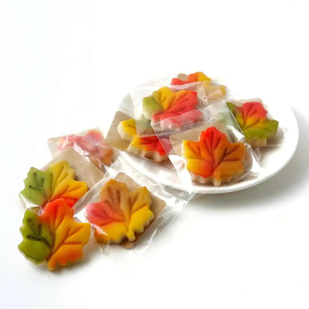 Gourmet Marzipan Autumn + Thanksgiving Maple Leaves Candy Colorful leaf-shaped cookies in clear packaging on a white plate against a white background