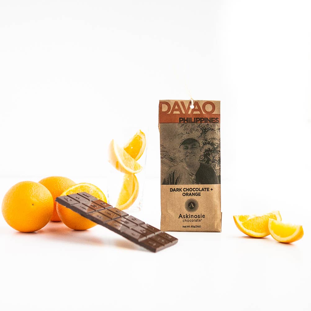 Wrapped and unwrapped dark chocolate bar with orange and orange peel on a white background