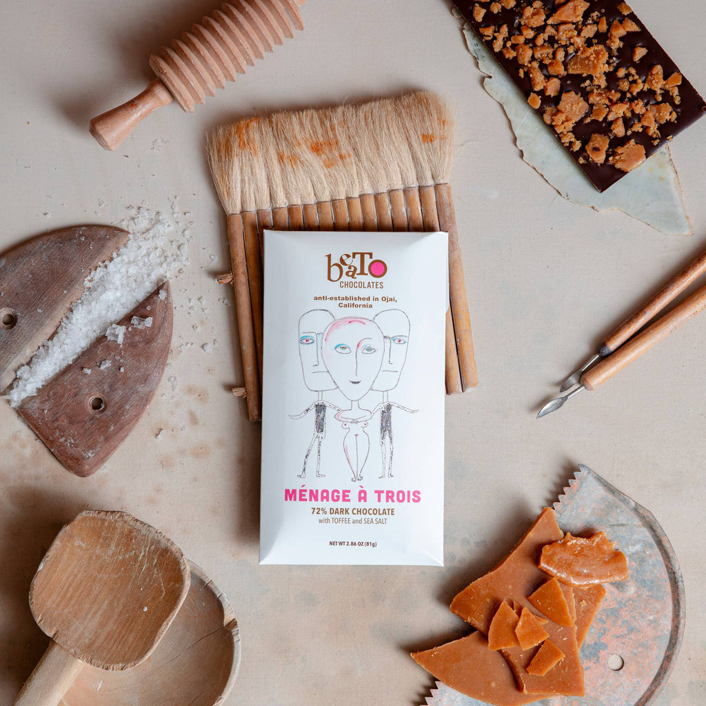 Beato Chocolates "Ménage à Trois" 72% Dark Chocolate with Toffee and Sea Salt lying on a table with painting implements nearby