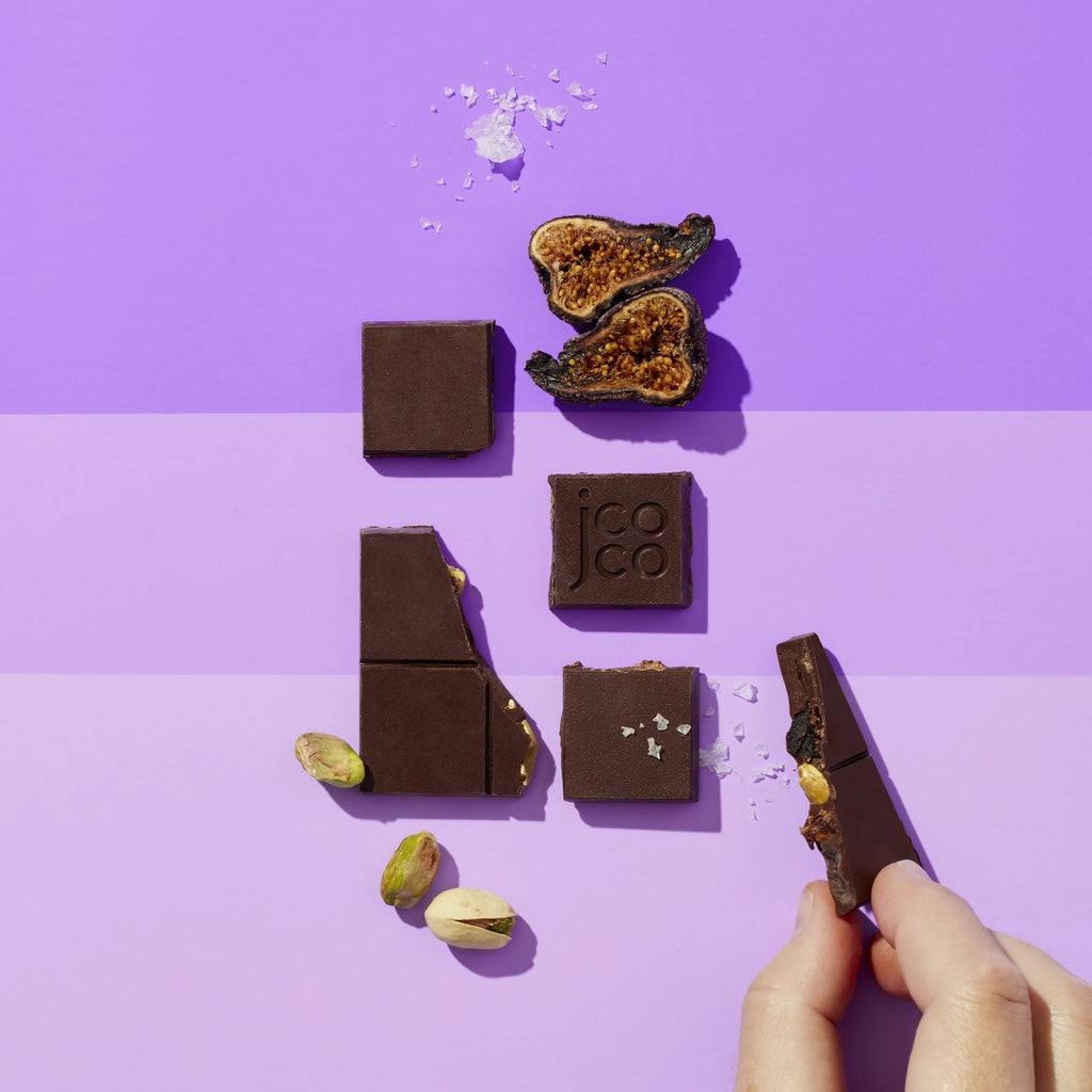 Pieces of Black Fig Pistachio 72% Mini on a table with three shades of purple