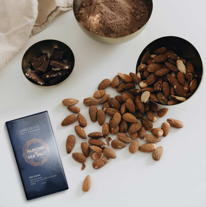 A wrapped Almond & Sea Salt Bar 75% bar next to its ingredients on a white table.