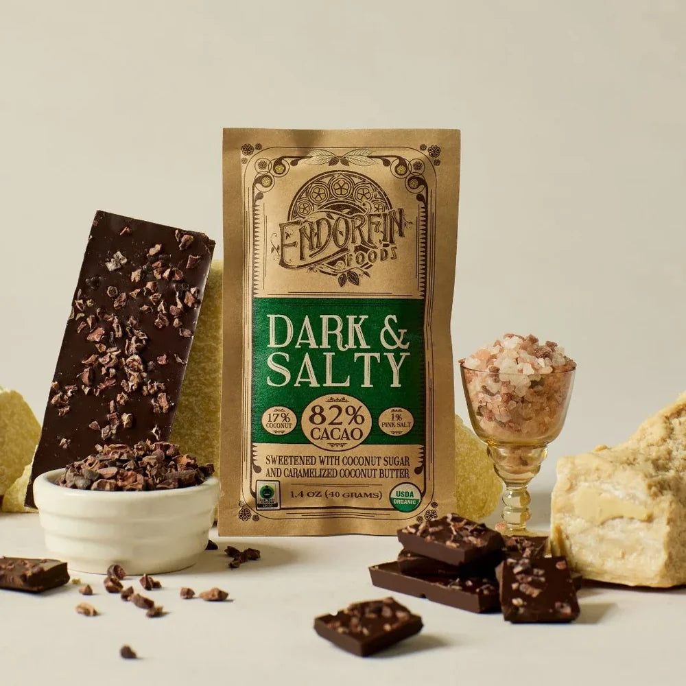 Coracao's Dark and Salty chocolate bar packaging with and open bar, chocolate pieces and ingredients on a neutral background