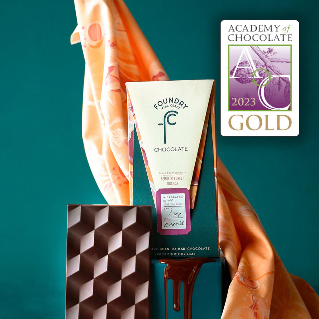 Foundry Chocolate bar against a scarf holding it against a teal background, featuring the Academy of Chocolate 2023 Gold award.