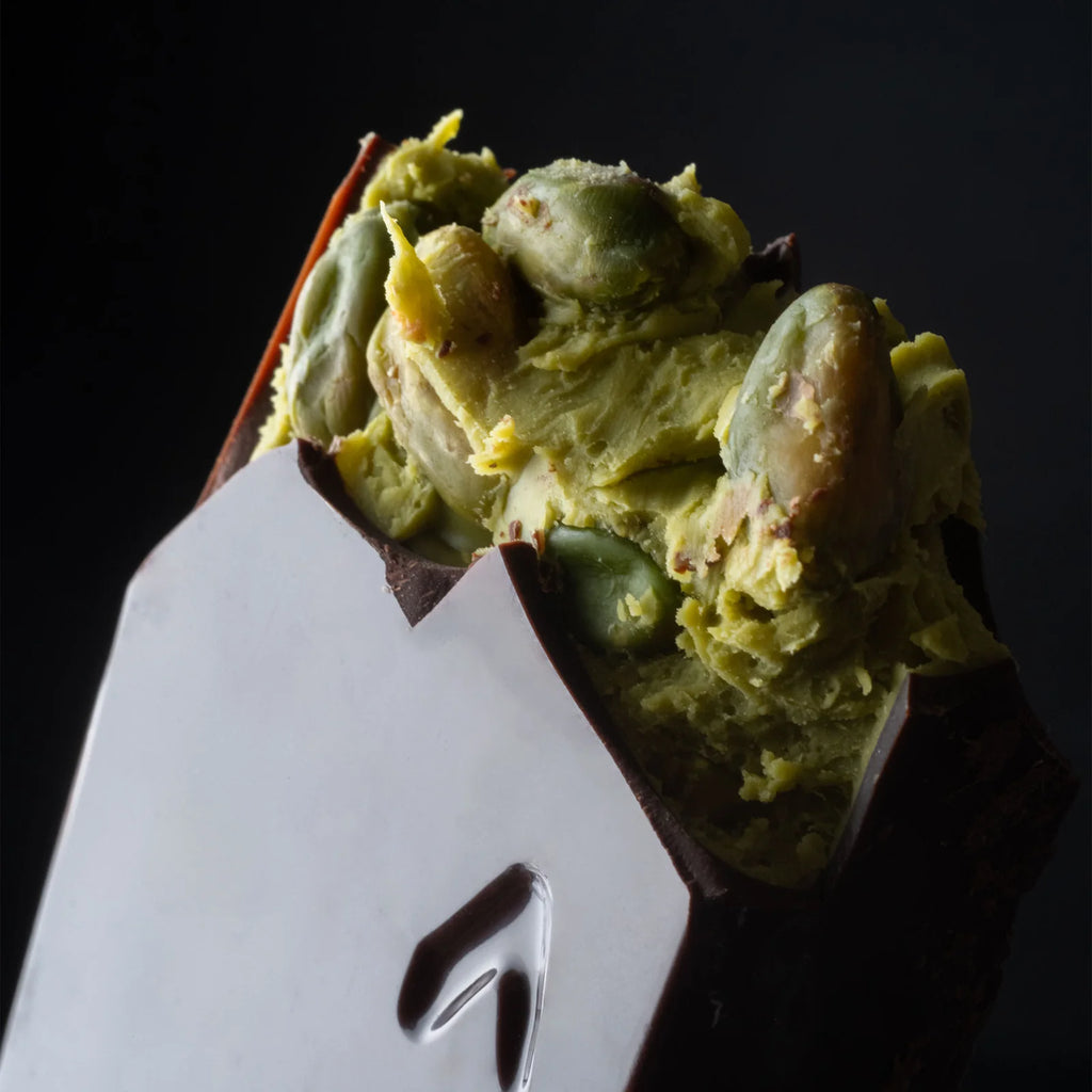 Close-up of an unwrapped piece of the 75% Dark Chocolate with Pistachio bar against a black background