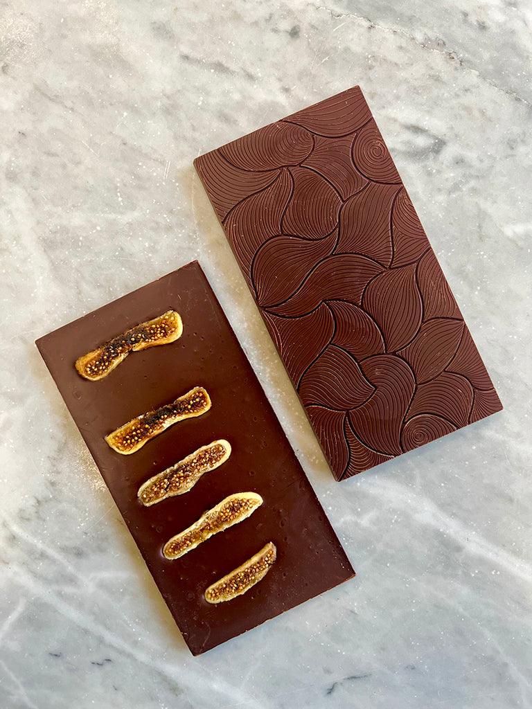 Two unwrapped 62% Dark w/ Figs, Star Anise & Cinnamon bars on a marble table