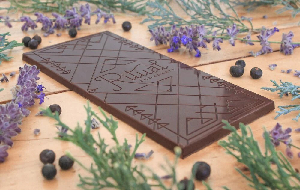 Unwrapped Ritual Chocolate Juniper Lavender Chocolate Bar against a wood table with juniper berries and lavender