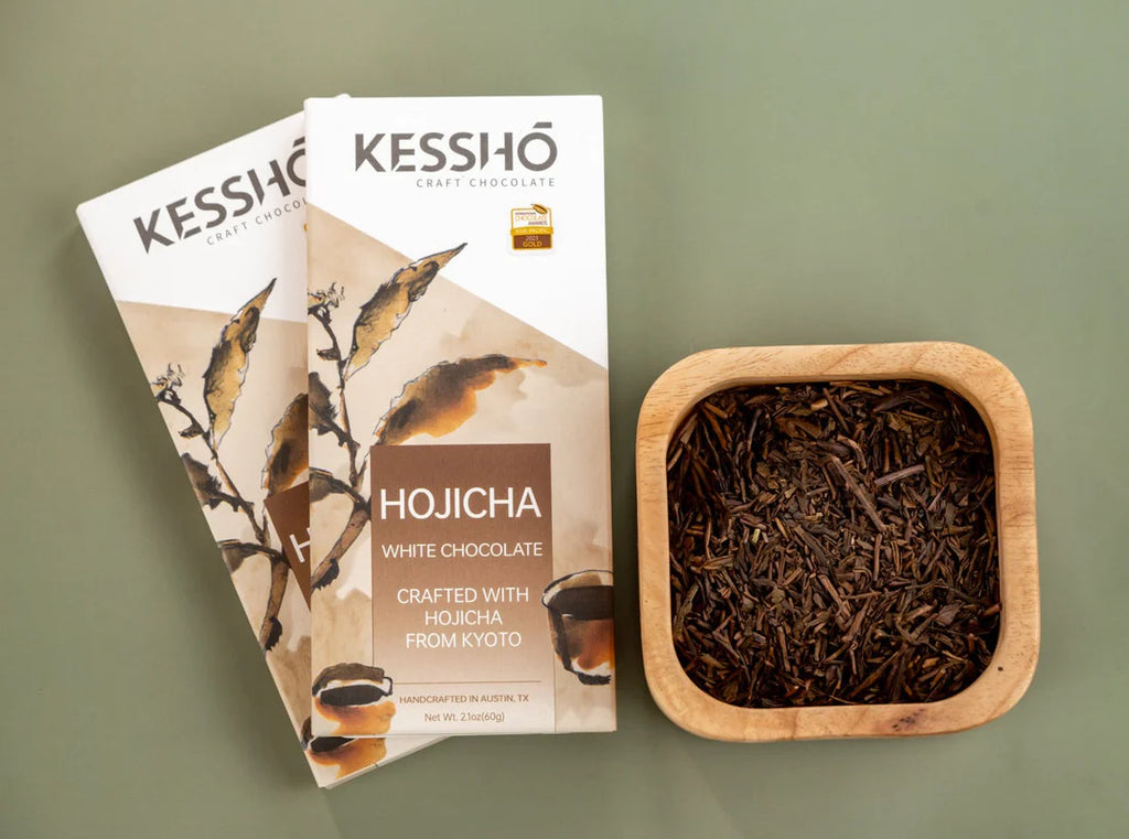 Two KESSHO Hojicha White Chocolate Bars with a bowl of tea leaves
