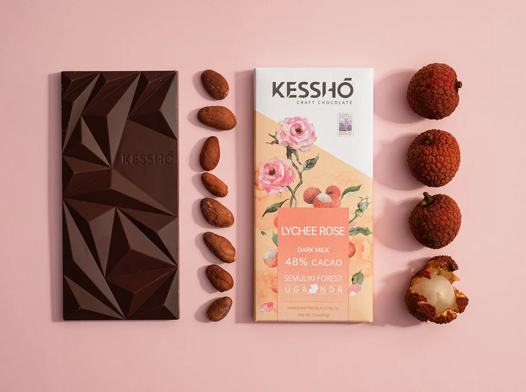The front of a KESSHO wrapped Lychee Rose 48% Dark Milk Cacao bar with lychees and roasted cacao beans and a chocolate bar