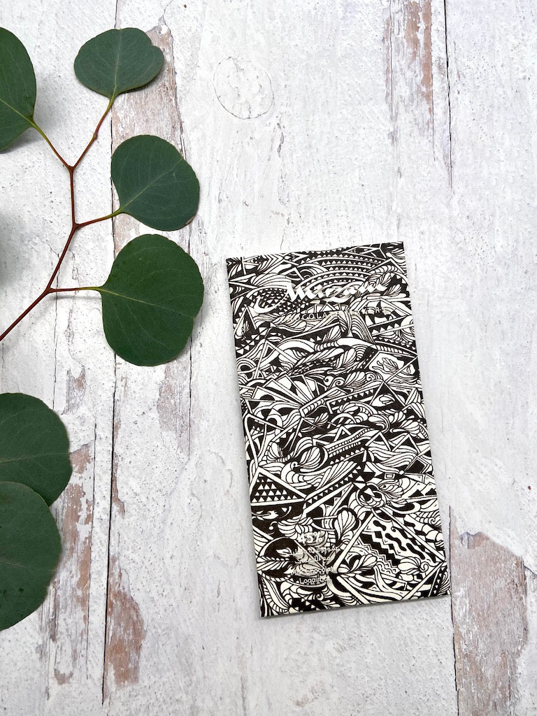 A wrapped Loqaimat Milk Chocolate Puffed Quinoa with Date Syrup bar on a wooden table with leaves