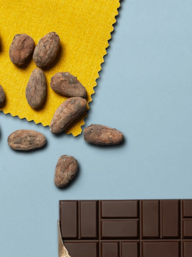 Zoomed in photo of a partially opened 85% Cacao - Brazil bar on a blue table with cocoa beans