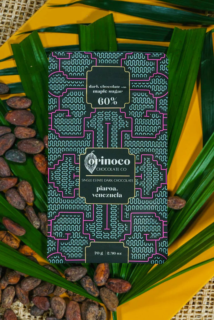 Piaroa, Venezuela 60% Dark Chocolate laying on a yellow table with cocoa beans and leaves