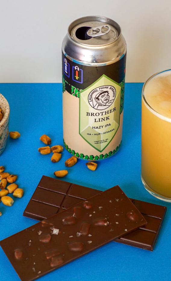 Two unwrapped Beer Snacks 53% bars on a blue table with a can of beer, corn nuts, and a glass of beer