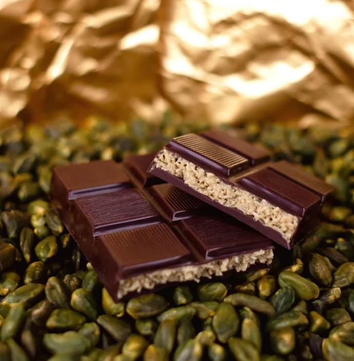 Chocolate bar with a crumbly center on green seeds with gold leaf in the background