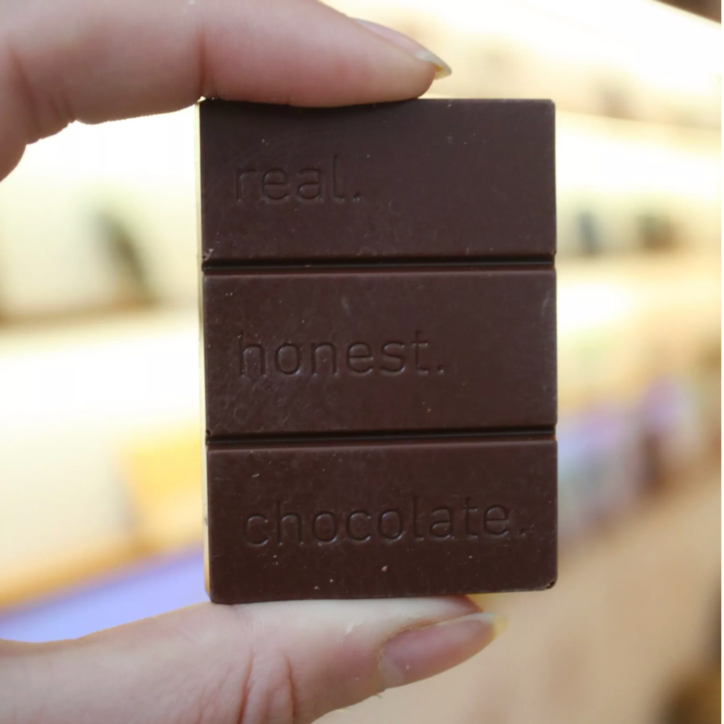 Two fingers holding choclate bar that  says real honest chocolate against a burry background