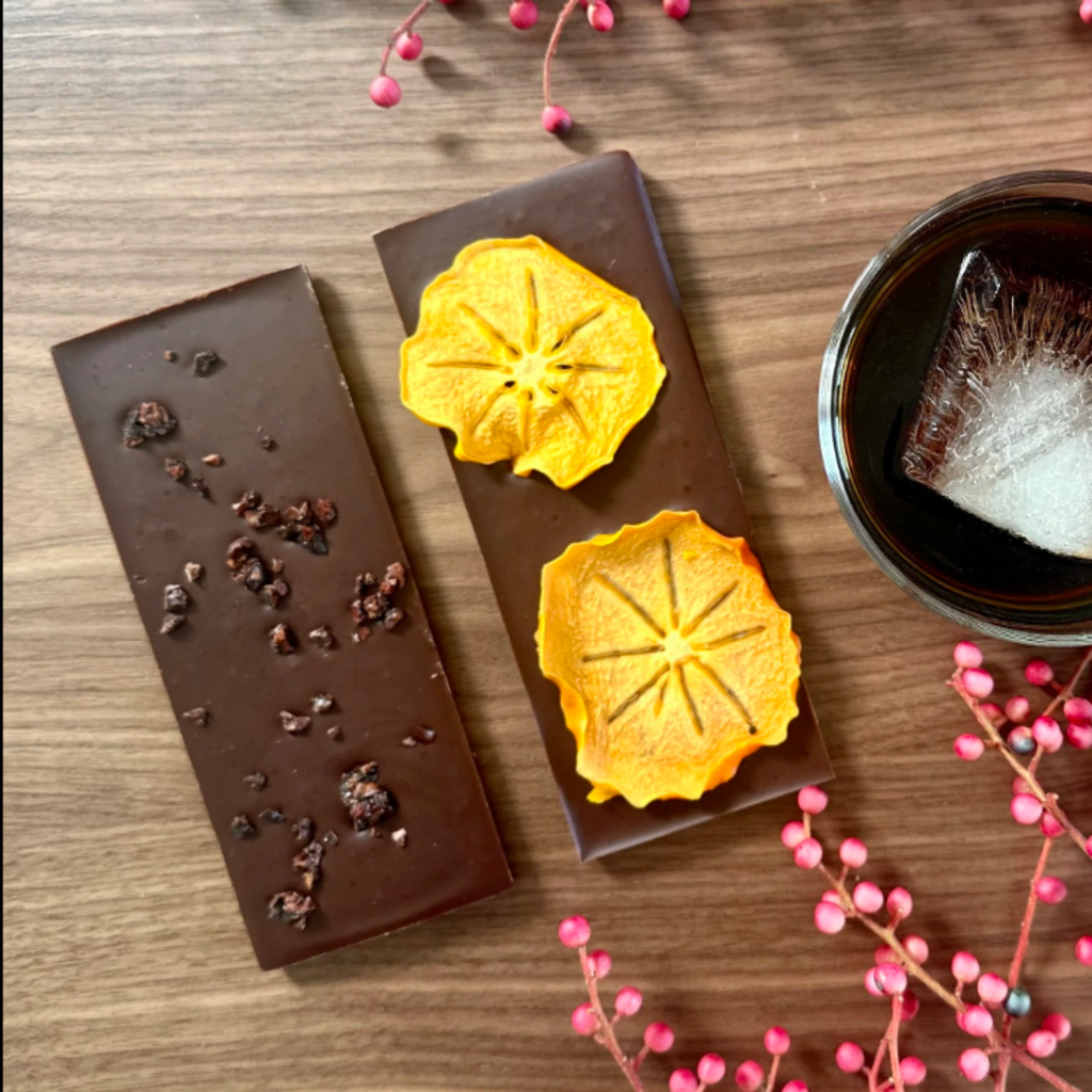 J Street 72% NOCINO NIB/FUYU Chocolate bars with decorative elements and a cup of tea on a wooden surface with pink flowers