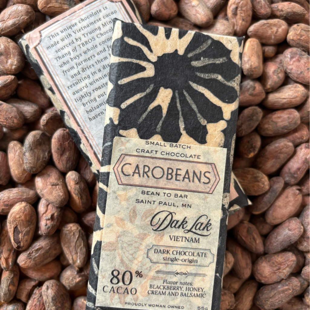 Carobeans Dak Lak Vietnam 80% cacao bar packaging against a bed of cacao beans