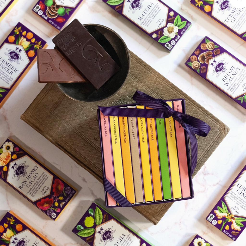 Mini Exotic Chocolate Bar Library gift set with two chocolate bars in a bowl sitting on top of a wood surface surrounded by misc. chocolate bars