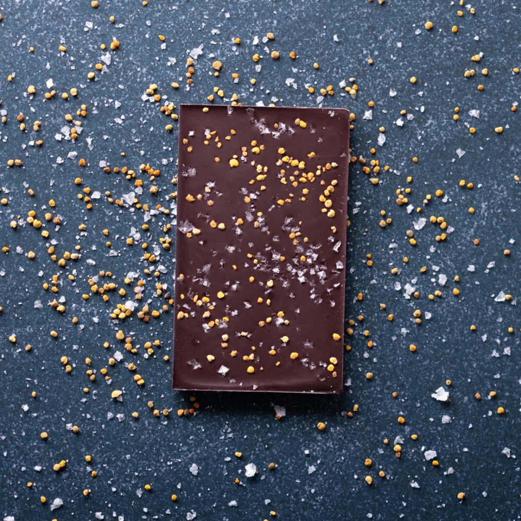Unwrapped 70% Uganda with Bee Pollen and Salt bar on a dark table with bee pollen and sea salt