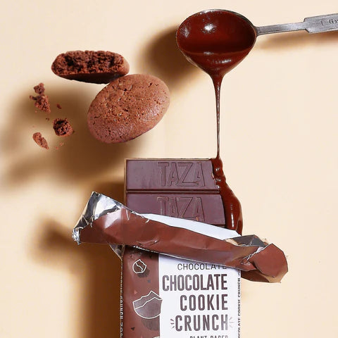 Partially unwrapped Chocolate Cookie Crunch Bar 70% - Vegan with two chocolate cookies above it, and a spoon filled with chocolate pouring melted chocolate onto the bar