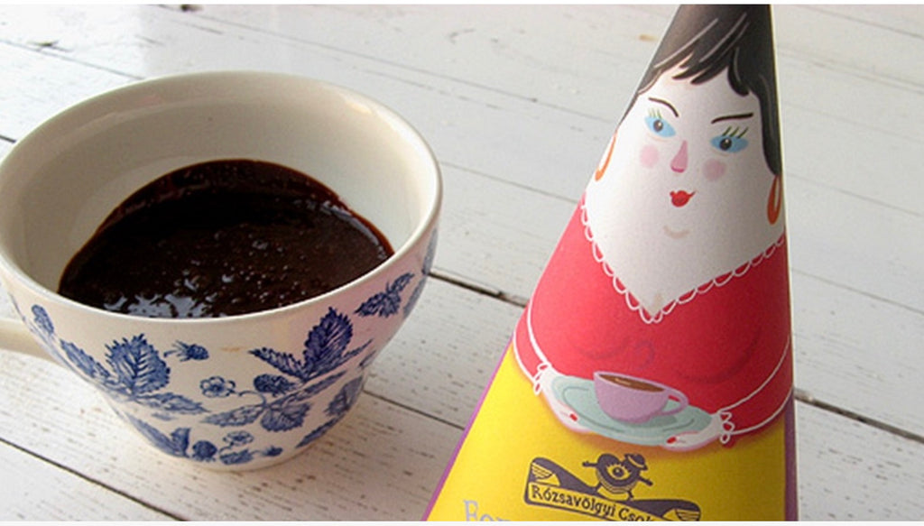 A blue and white  cermanic cup filled with drinking chocolate next to a package of Rozsavolgyi Lavender Drinking Chocolate on a wood background