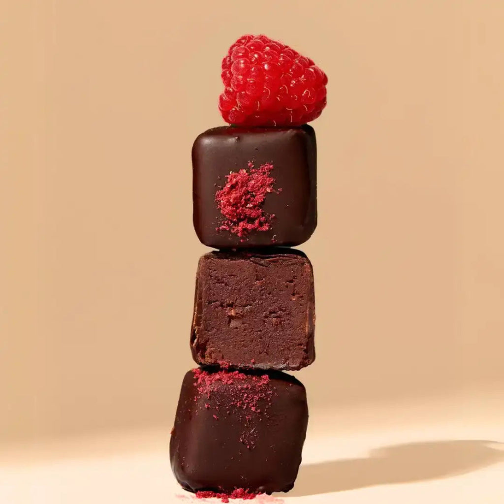 Stack of chocolate truffles with a raspberry on top against a beige background