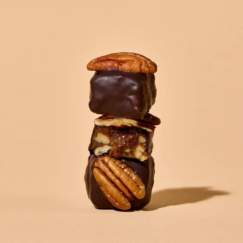 Stack of chocolate-dipped dates with pecans on a beige background