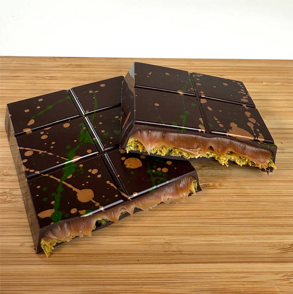 Two unwrapped pieces of Dubai Done Better: Pistachio Caramel bars on a wooden table