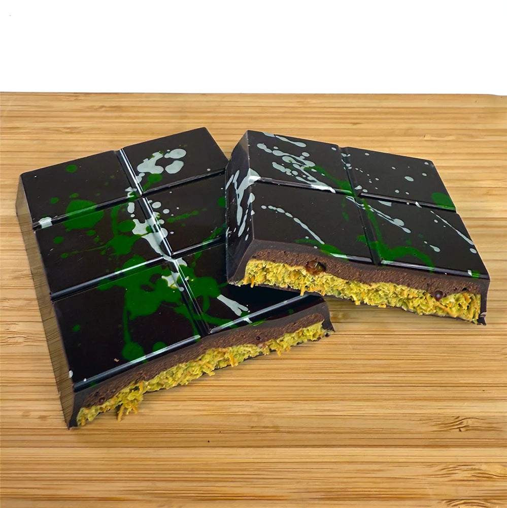 Two unwrapped pieces of the Dubai Done Better: Pistachio Bittersweet Ganache bar on a wooden table