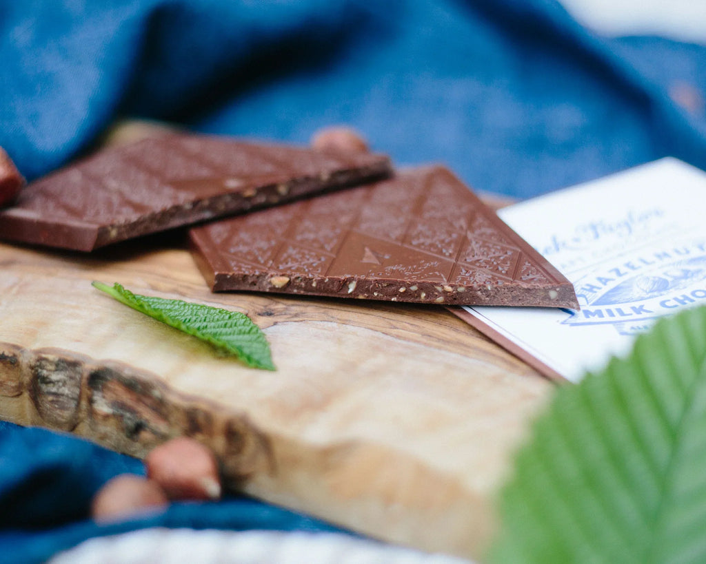 Two pieces of a Milk Chocolate with Hazelnuts 55% bar from Dick Taylor on a wooden cutting board