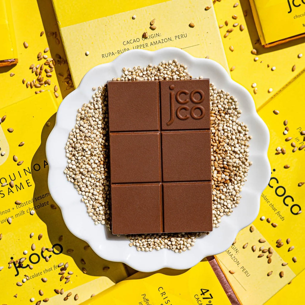 Jcoco Crisp Quinoa Sesame Milk Chocolate 47% Mini in a white bowl of quinoa on a yellow table 