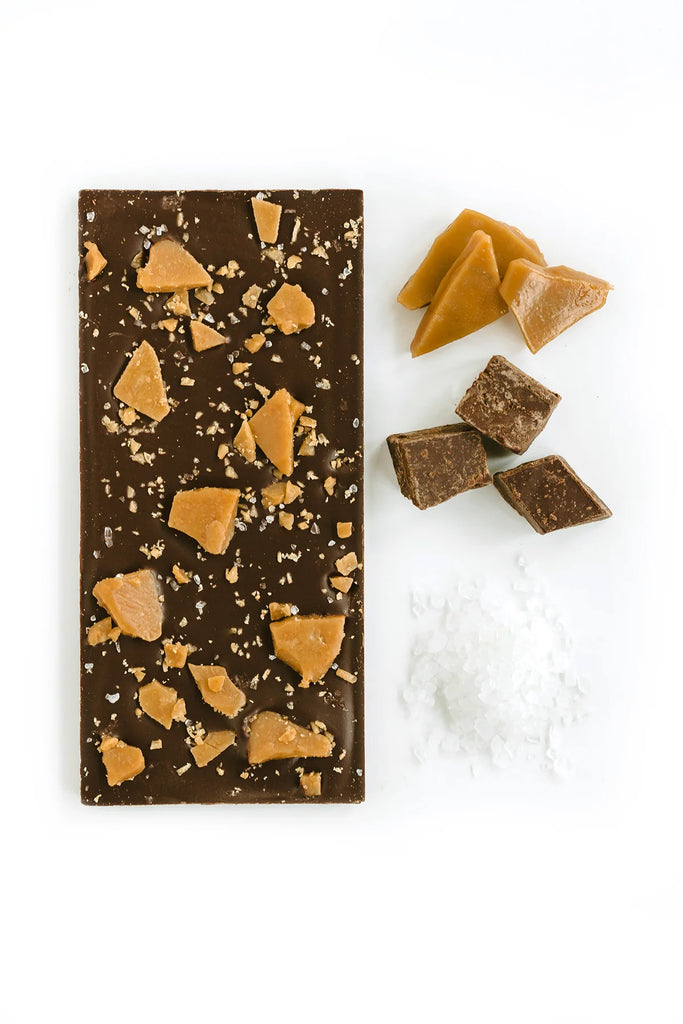 Unwrapped Toffee Talk against a white background with sea salt, pieces of chocolate, and pieces of toffee