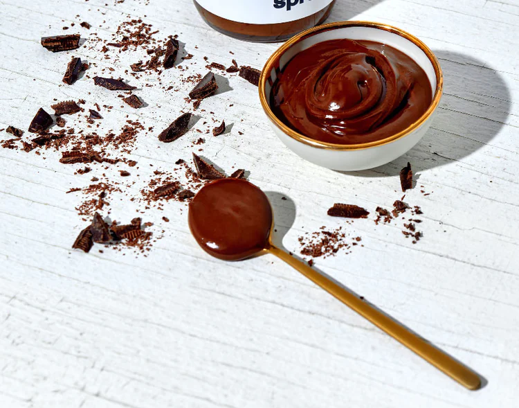A cup of Dark Chocolate Hazelnut Butter on a table with a spoon full of the butter next to it.